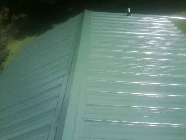 New green metal panels meeting at the ridge of a roof — Flat Roof Repair work by our crew in Lykens