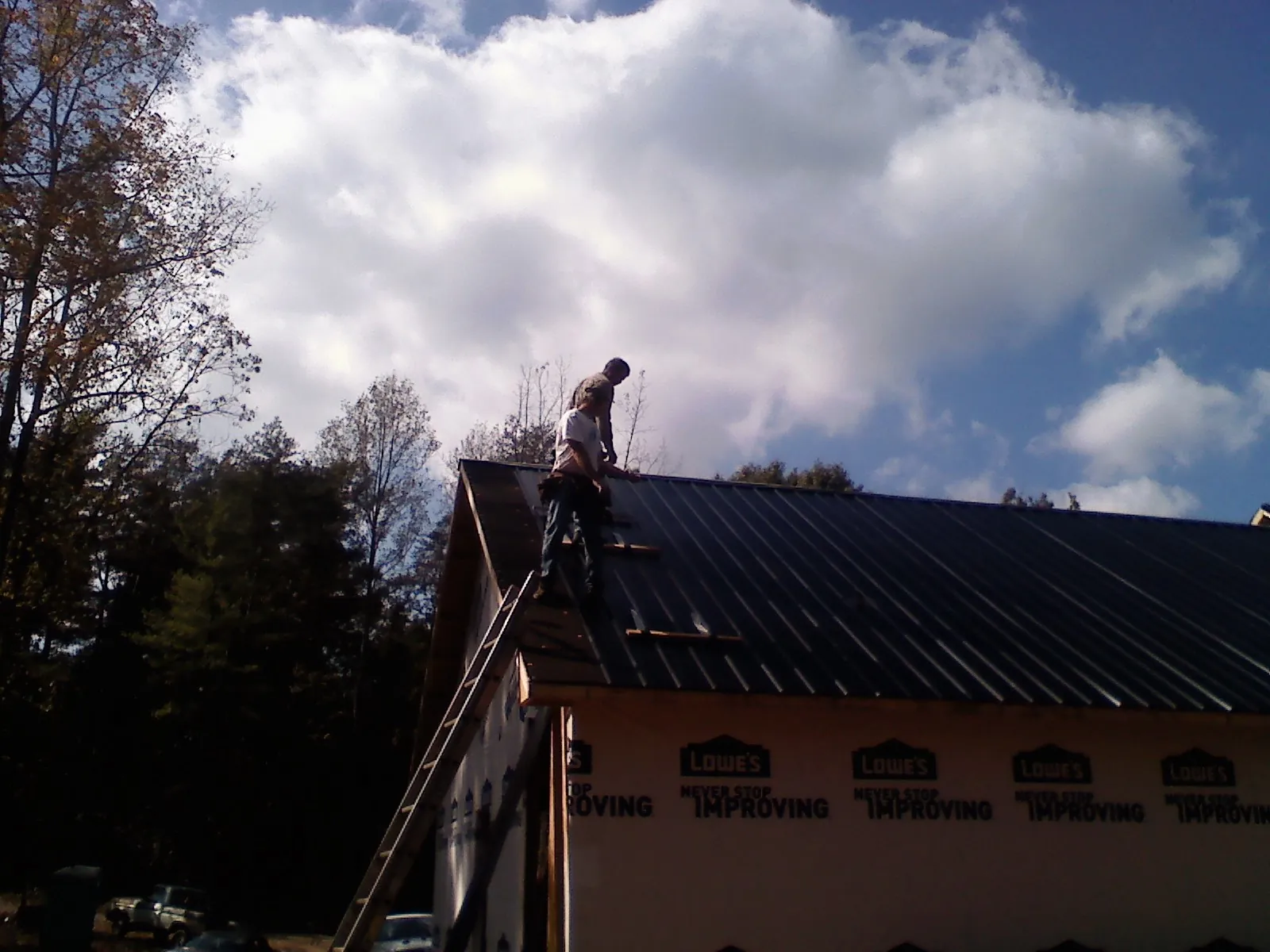 Roofer fastening dark metal panels high against a cloudy sky, from a Roof Inspection job in Lykens