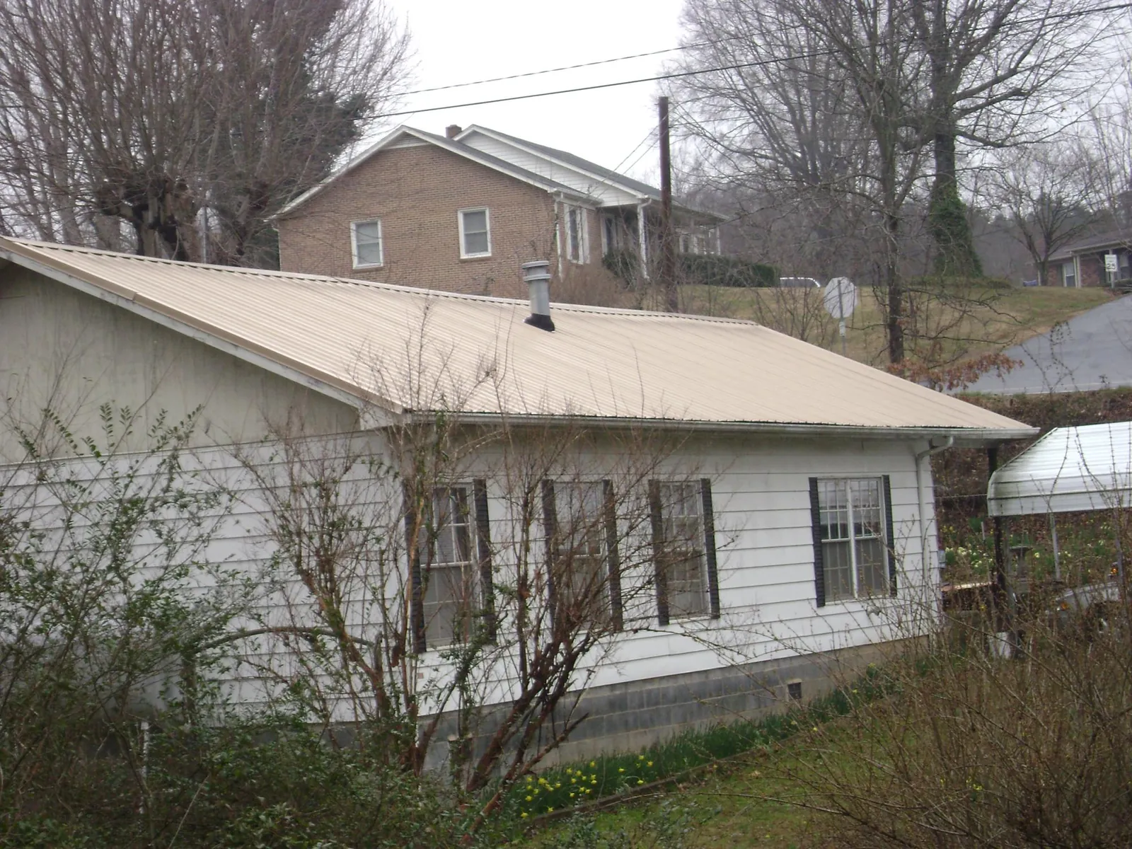 Tan metal roof on a white sided house set into a hillside — Commercial Roofing by Roofing Brothers in Lykens
